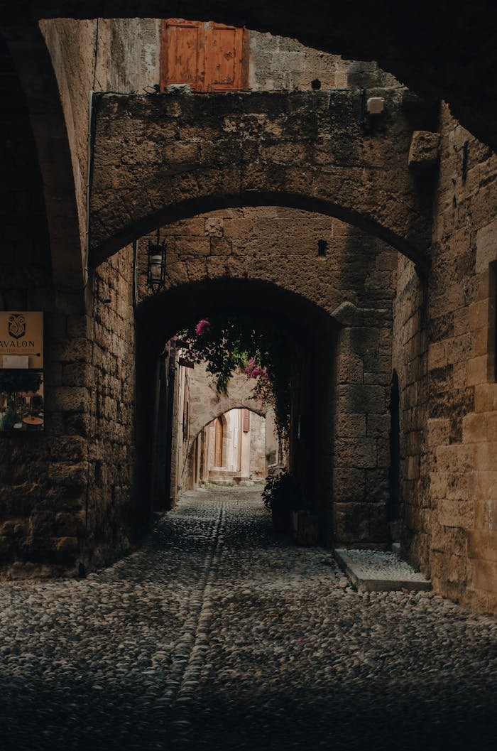 Explore a medieval cobblestone alley in Rhodes, Greece, with stone arches and walls.